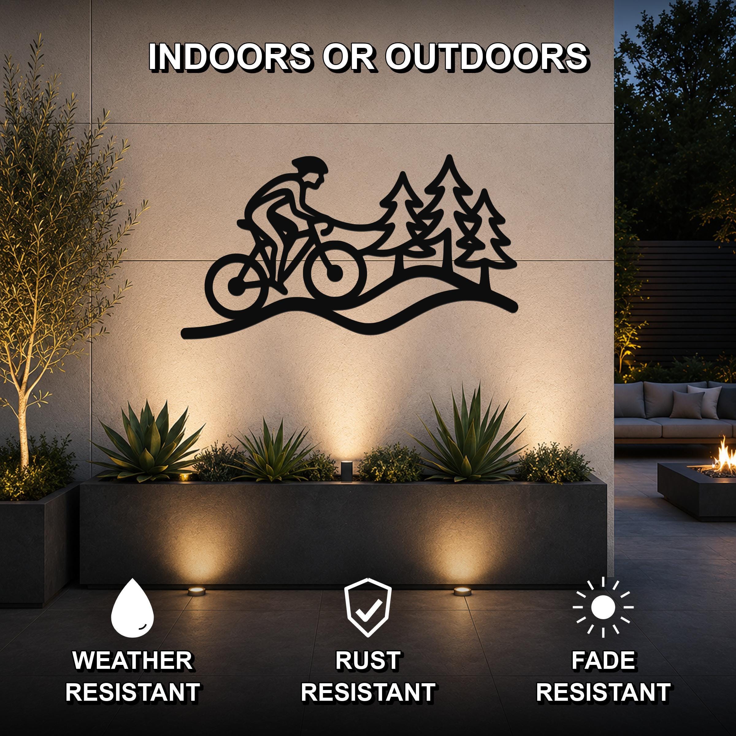 Black metal wall art featuring a cyclist silhouette and pine trees, mounted on an outdoor wall above a planter in a patio setting.
