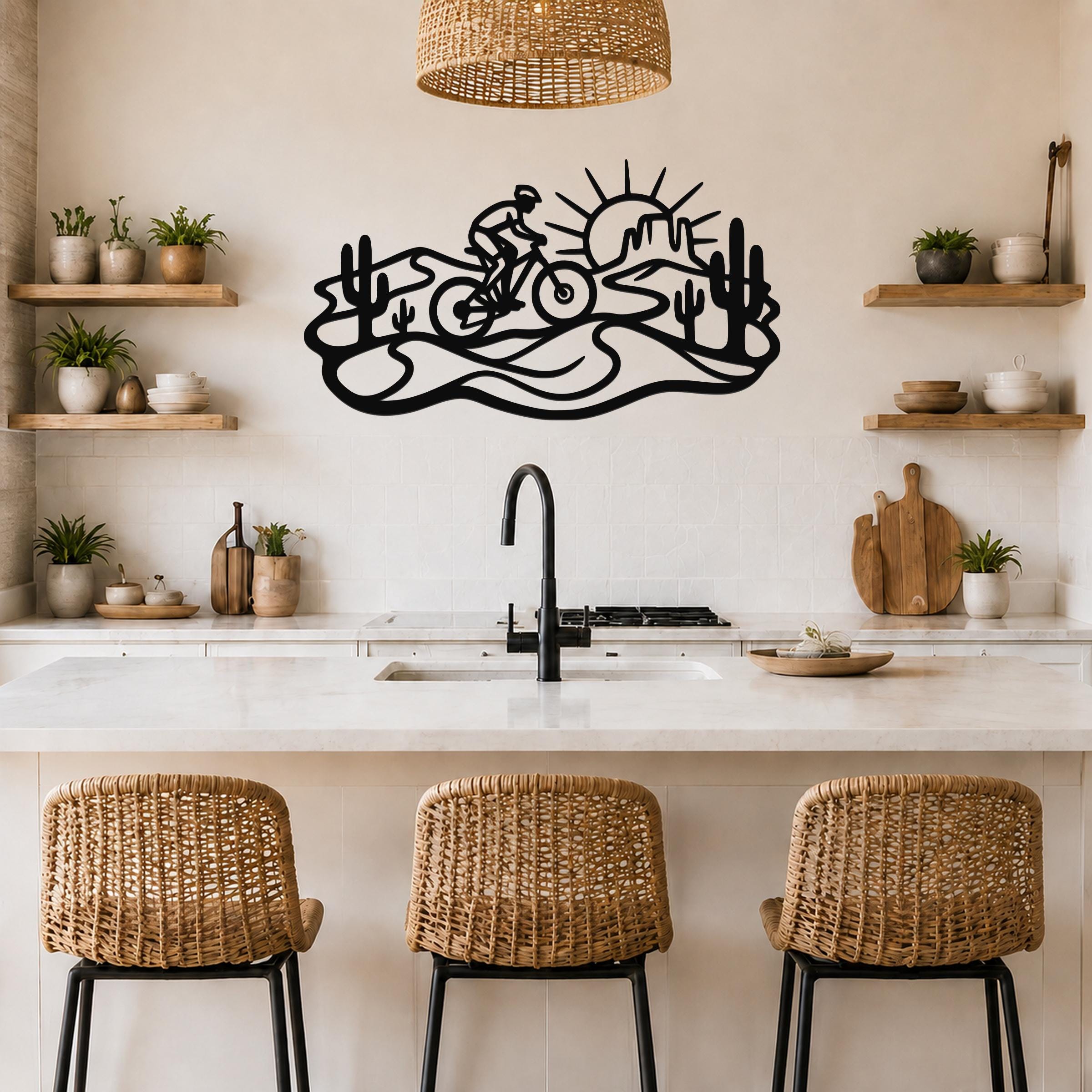Black metal wall art with a desert silhouette of a cyclist, cacti, and sun, mounted above a kitchen counter.