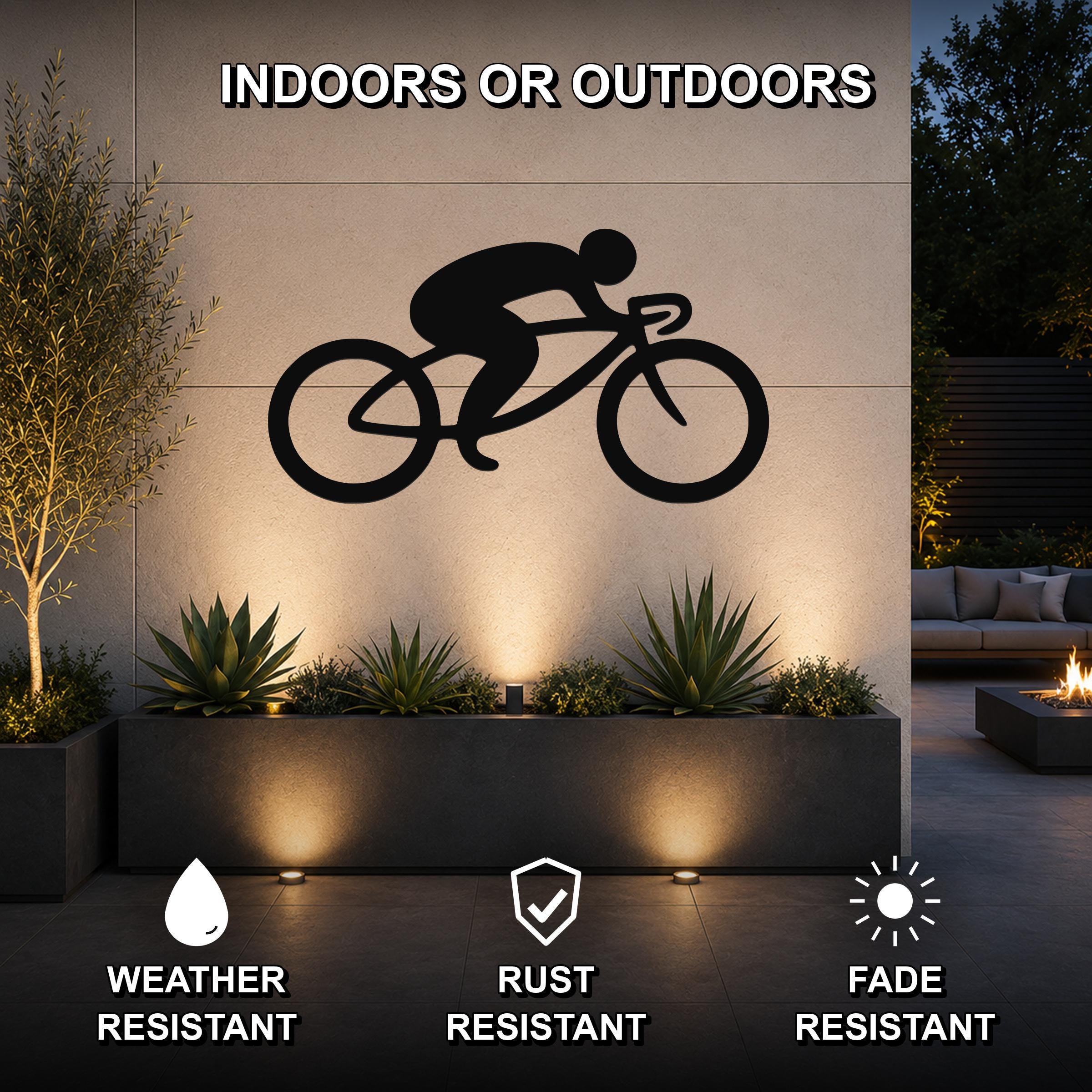Black metal cycling silhouette wall art mounted on an outdoor wall above a planter, featuring a minimalist design of a cyclist on a bike, shown in a modern patio setting with ambient lighting.