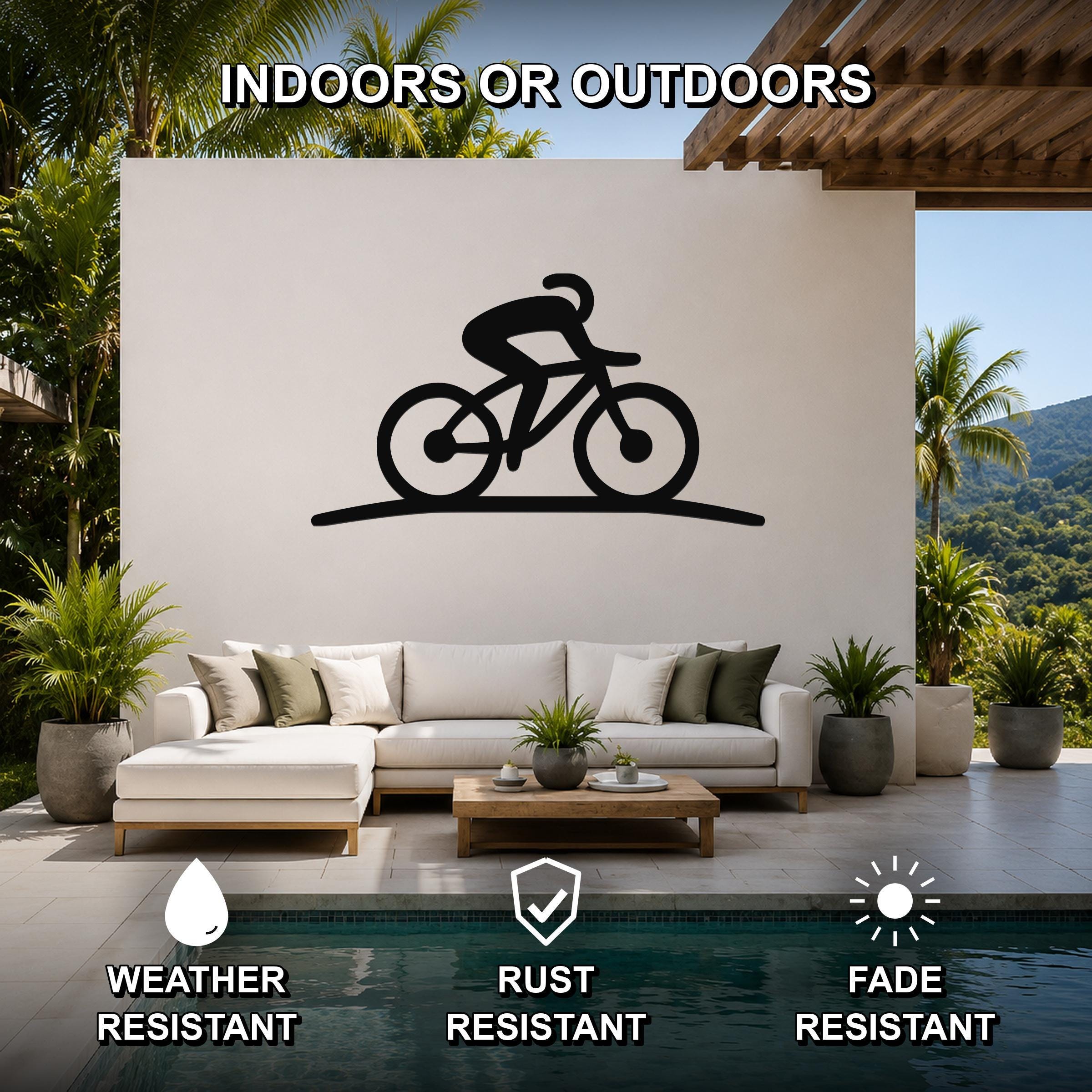 Black metal cycling silhouette wall art with motion-line cutouts, mounted on a white outdoor wall above a sofa in a patio living area.