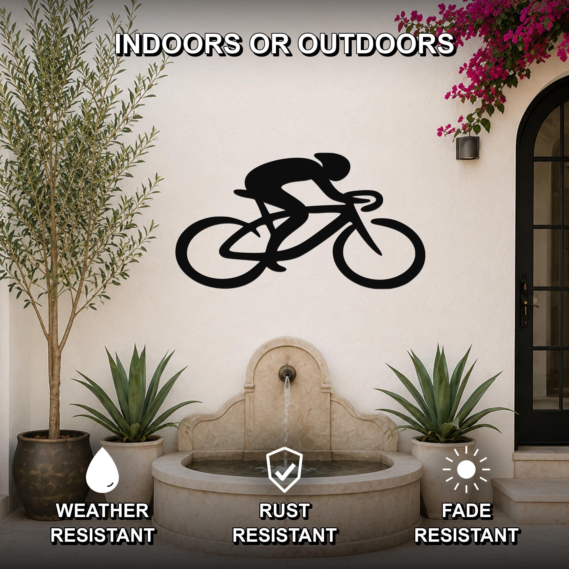 Black metal wall art featuring a cyclist silhouette on a bike, mounted on an outdoor wall above a stone fountain with potted plants and a flowering vine.