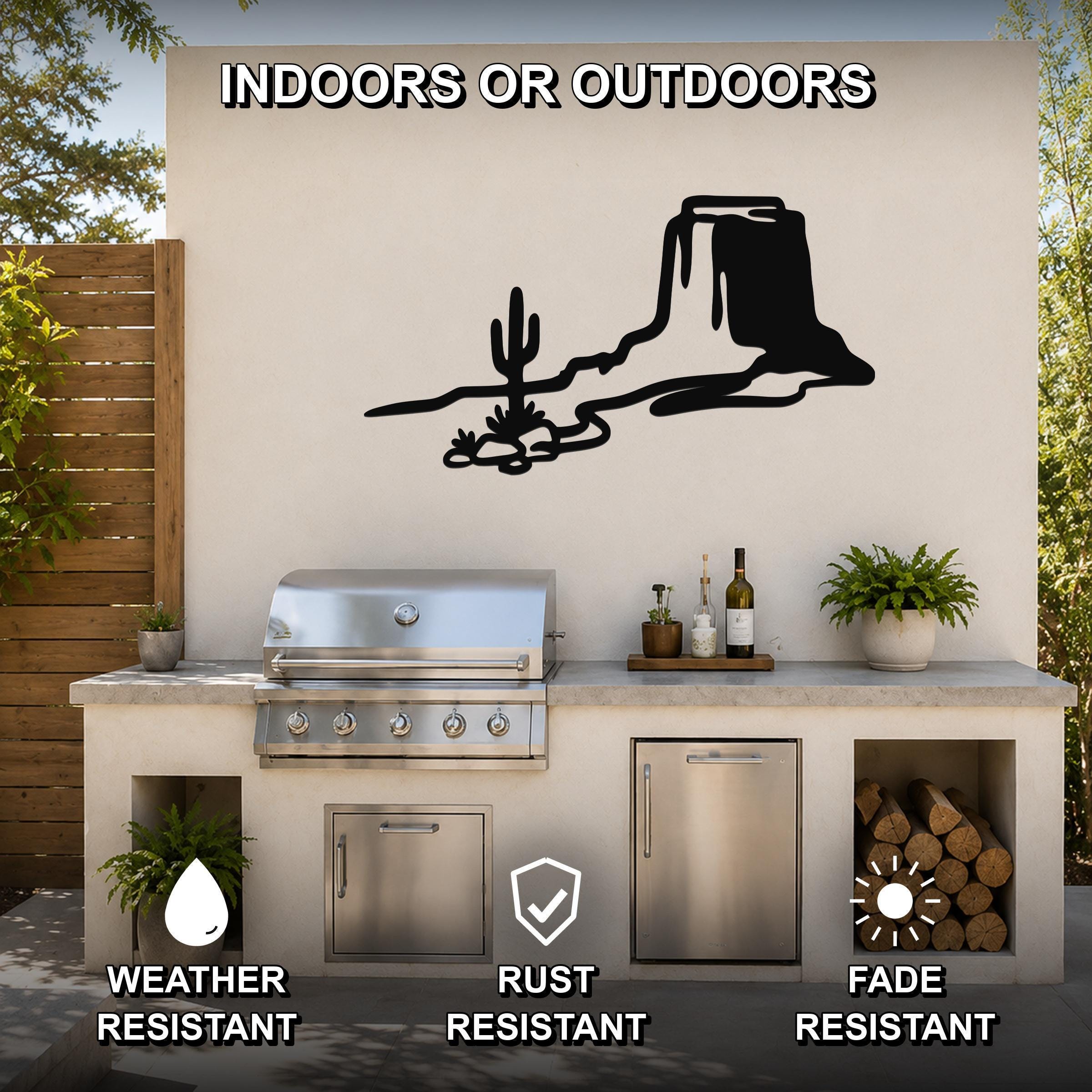 Black metal wall art featuring a bold silhouette of a desert mesa and cactus, mounted on an outdoor kitchen wall above a stainless steel grill.