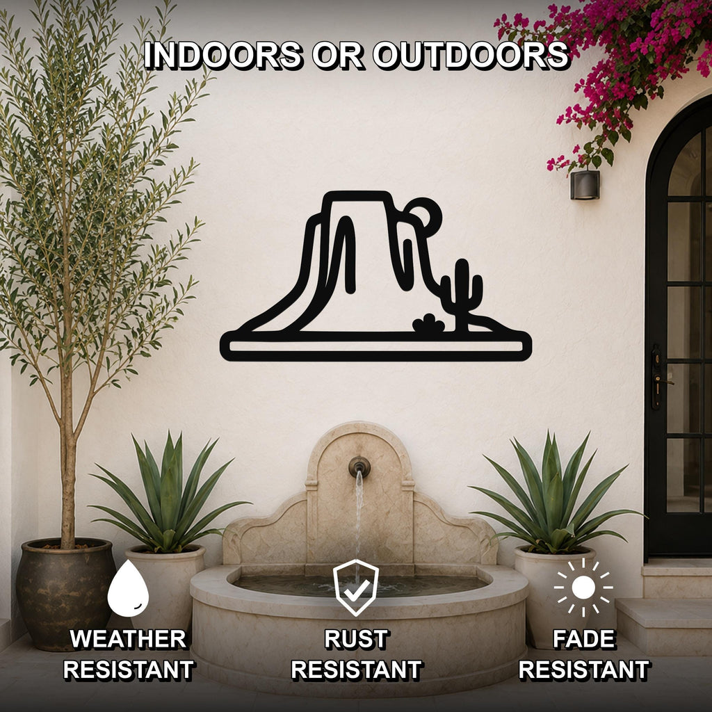 Black metal wall art silhouette of a desert mesa and cactus, mounted on an outdoor patio wall above a stone fountain.