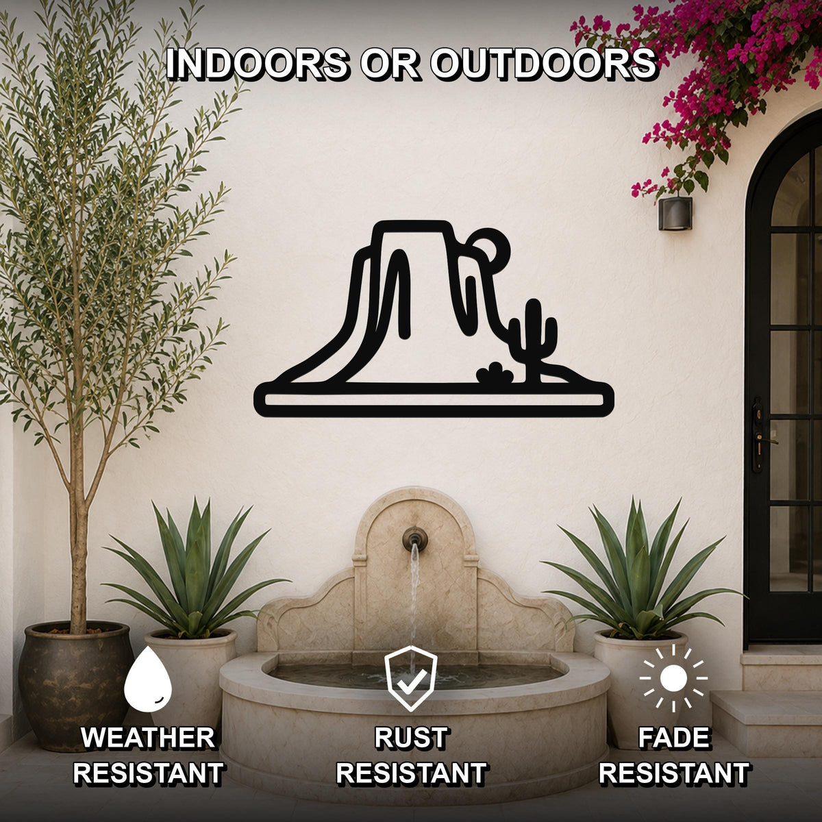 Black metal wall art silhouette of a desert mesa and cactus, mounted on an outdoor patio wall above a stone fountain.