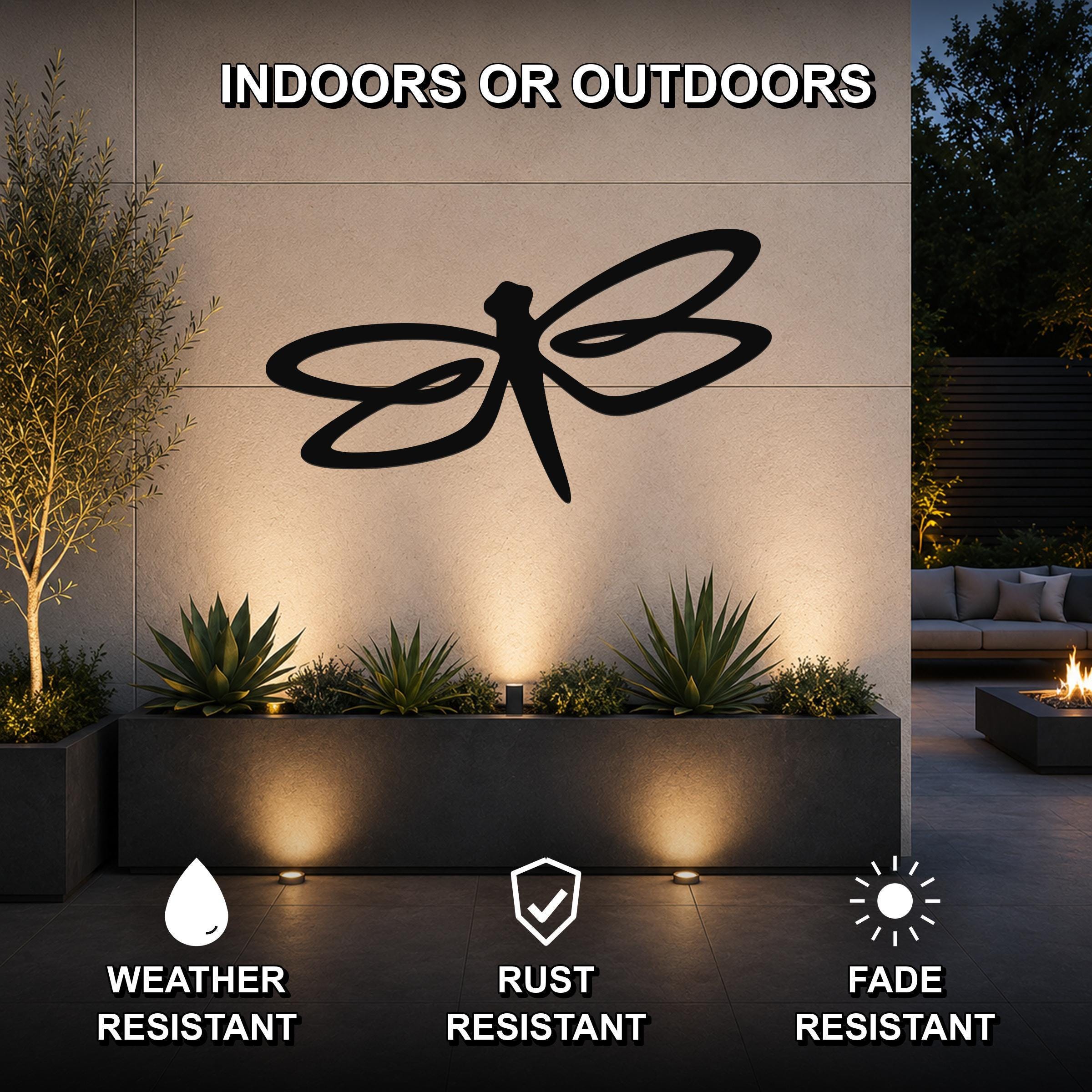 Black metal dragonfly wall art with flowing wing cutouts, mounted on an outdoor wall above a planter in a modern patio setting.