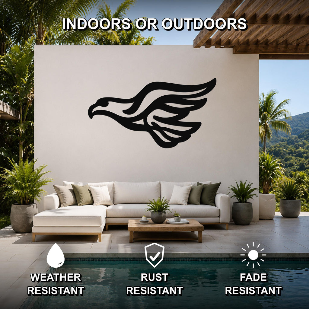 Black metal eagle silhouette wall art with wing motion lines, mounted on a white outdoor wall above a sofa in a patio living area.