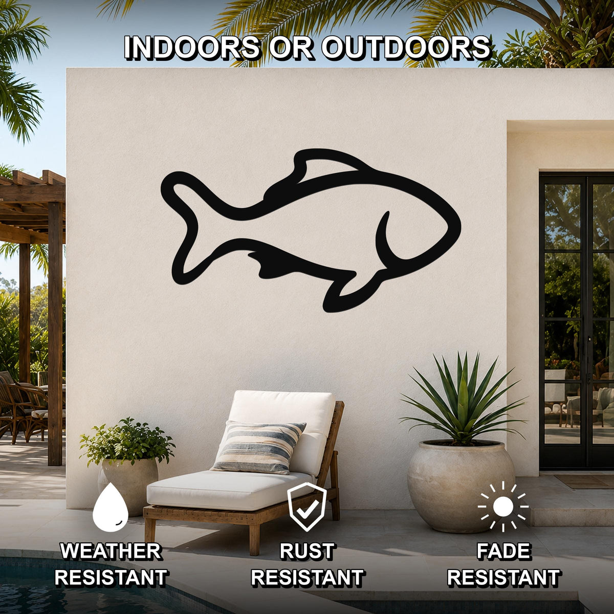 Black metal fish wall art with bold outline cutout, mounted on an outdoor patio wall above a lounge chair near a pool.