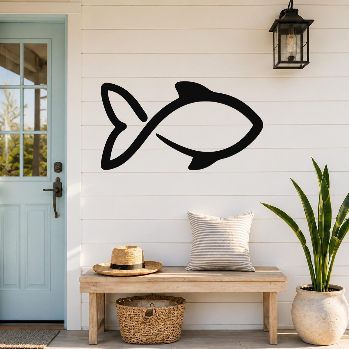 Black metal fish wall art with a simple silhouette design, mounted on a white shiplap wall above a wooden bench in a porch entryway.