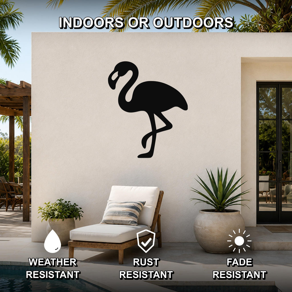 Black metal flamingo wall art silhouette mounted on an outdoor patio wall above a lounge chair, with palm trees and a pool visible in the background.