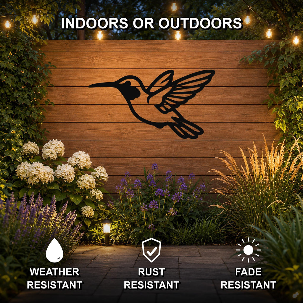 Black metal hummingbird wall art with wing and tail cutouts, mounted on a wooden fence in a garden with string lights and plants.