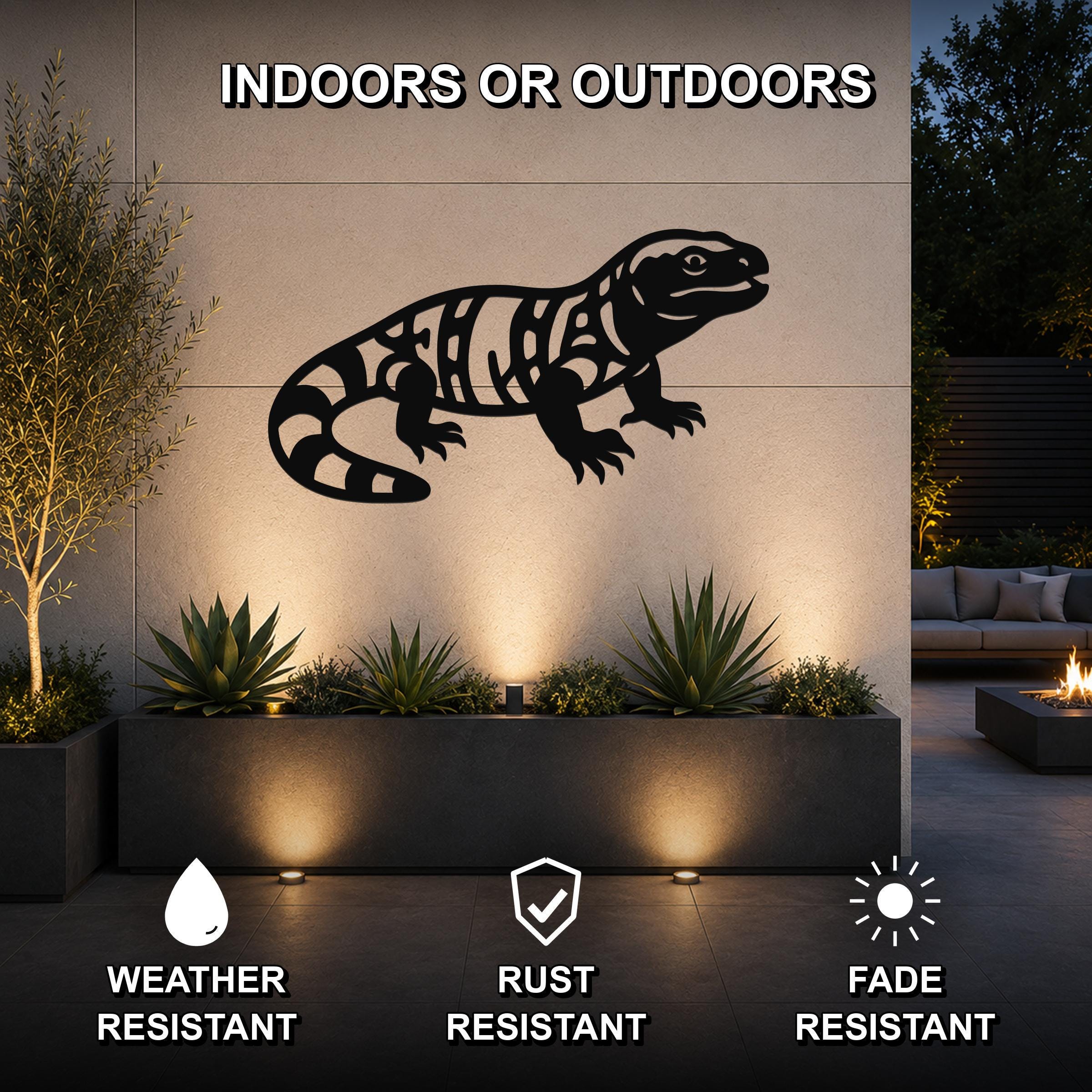 Black metal Gila monster wall art with intricate internal cutouts, mounted on an outdoor wall above a planter in a modern patio setting.