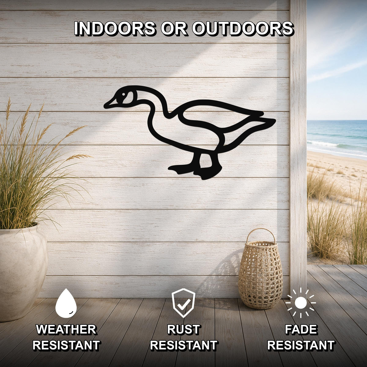 Black metal goose silhouette wall art mounted on a light wood plank wall, shown in an indoor-outdoor setting with a beach view, weather resistant, rust resistant, and fade resistant.
