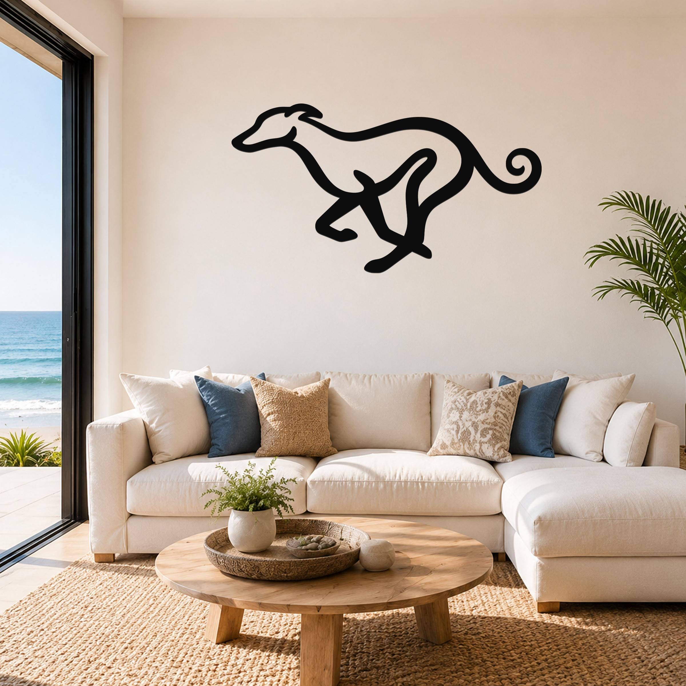 Black metal greyhound wall art in a running silhouette, mounted above a white sofa in a living room with ocean views.