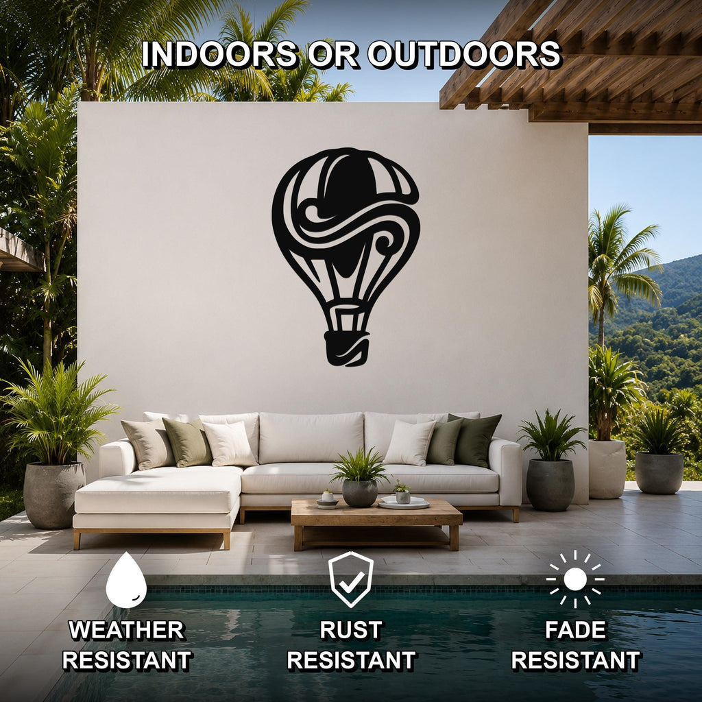 Black metal hot air balloon wall art with swirling cutout design, mounted on a white outdoor wall above a sofa in a patio living area.