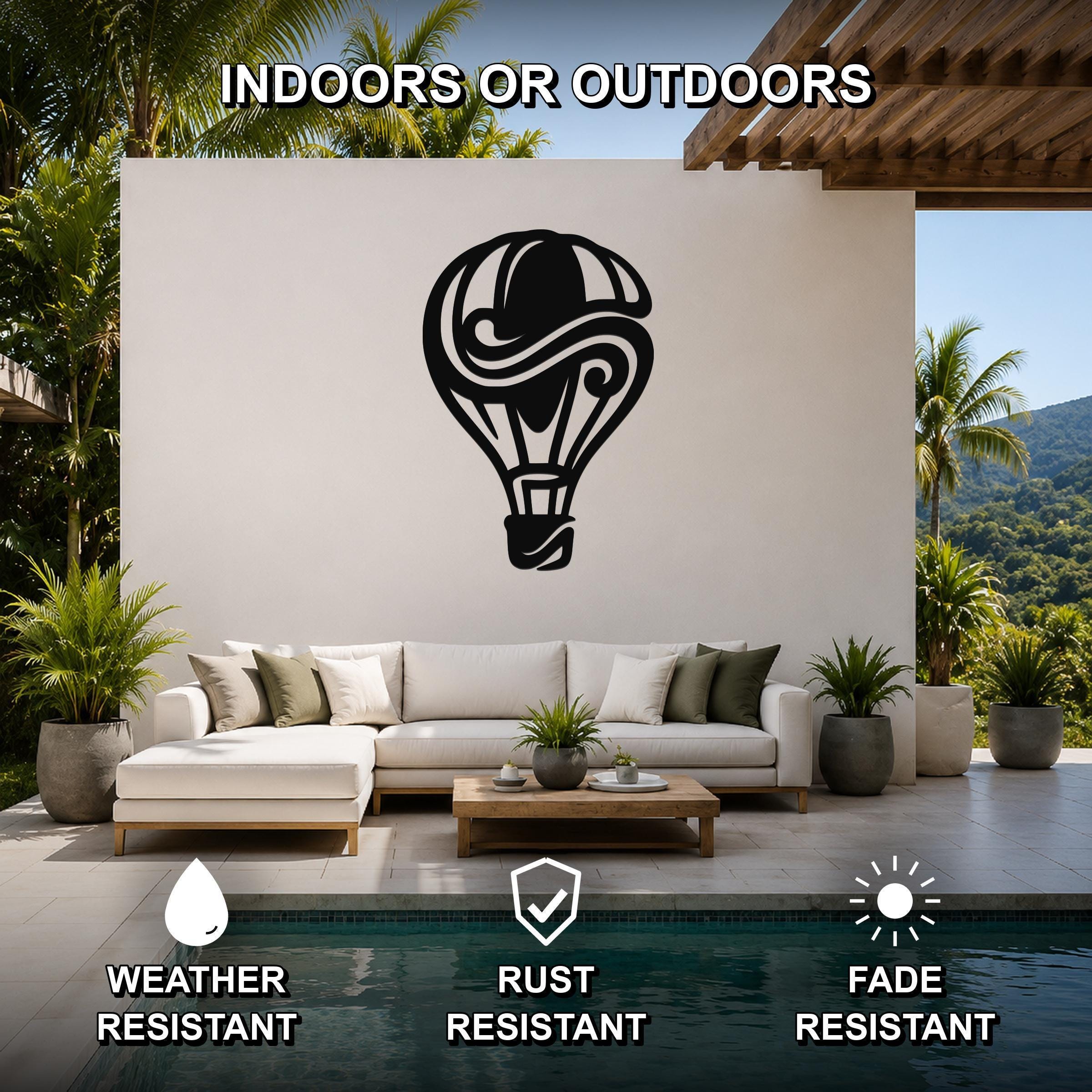 Black metal hot air balloon wall art with swirling cutout design, mounted on a white outdoor wall above a sofa in a patio living area.