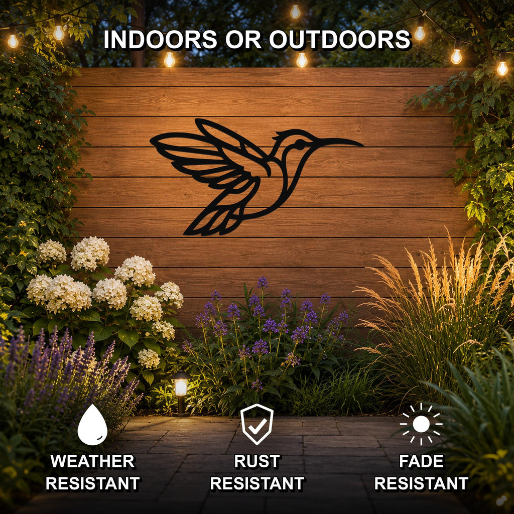 Black metal hummingbird wall art with motion-line cutouts, mounted on a wooden outdoor wall above a garden bed with flowers and string lights.