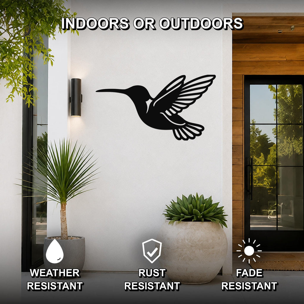 Black metal hummingbird wall art with wing and tail cutouts, mounted on a white exterior wall beside a glass door and potted plants.