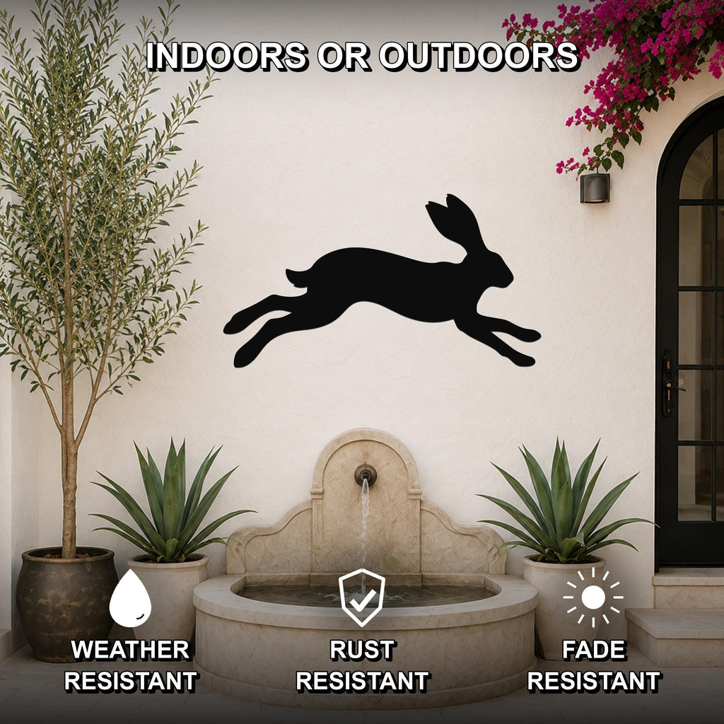Black metal jackrabbit wall art silhouette mounted on an outdoor wall above a stone fountain, flanked by potted plants and a flowering vine.