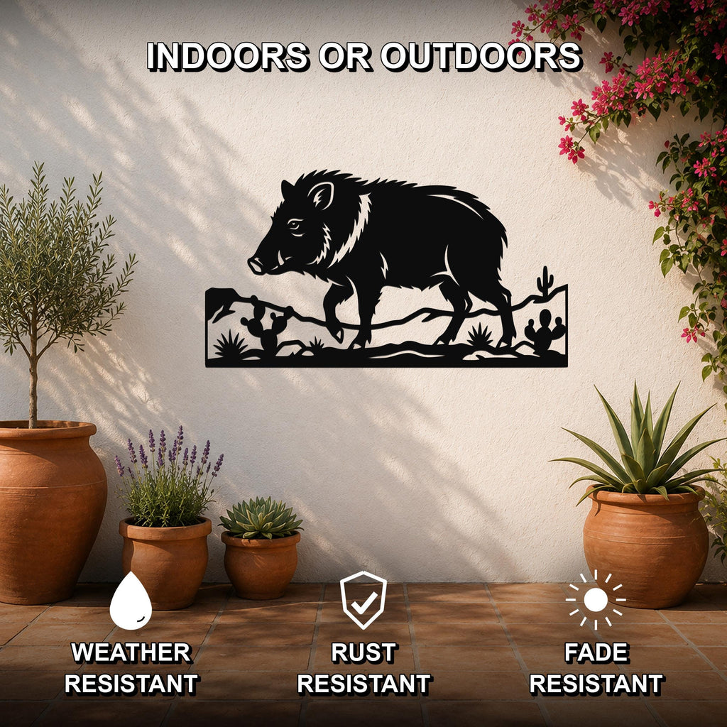 Black metal wall art featuring a javelina silhouette with cacti and desert landscape cutouts, mounted on an outdoor patio wall above potted plants.