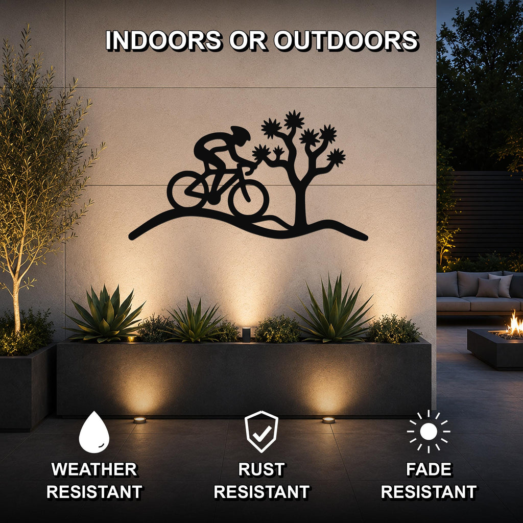 Black metal wall art featuring a cyclist silhouette riding past a Joshua tree, mounted on an outdoor wall above a planter in a modern patio setting.