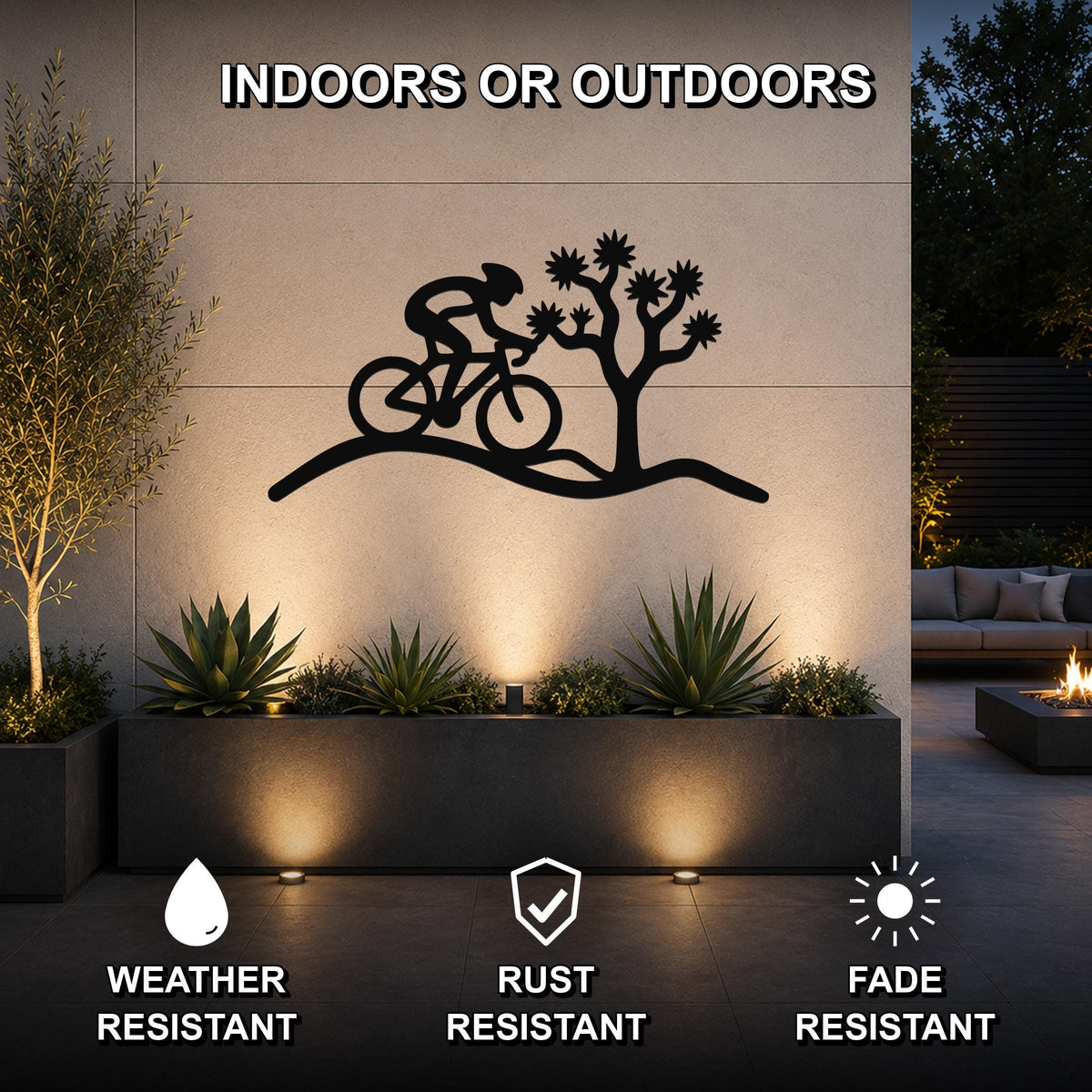 Black metal wall art featuring a cyclist silhouette riding past a Joshua tree, mounted on an outdoor wall above a planter in a modern patio setting.