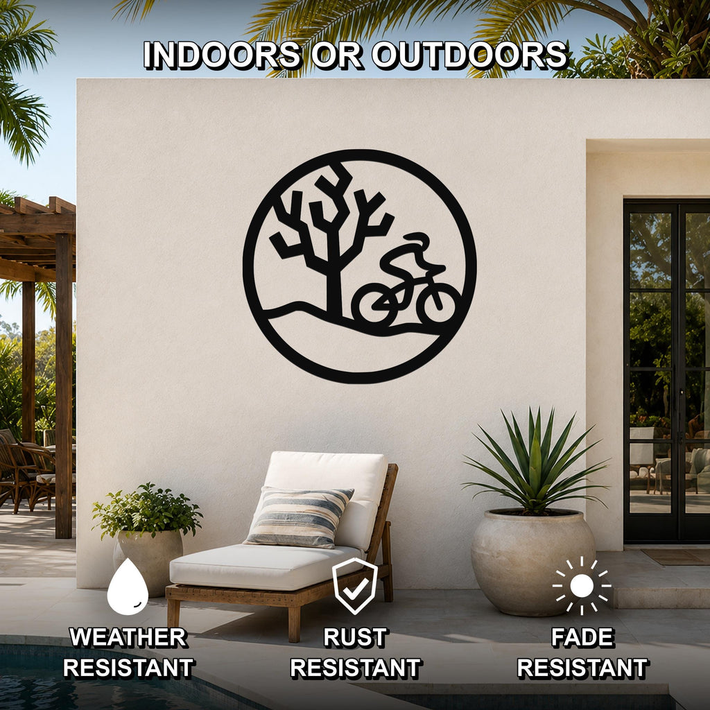 Black metal wall art featuring a circular silhouette of a cyclist and a Joshua tree, mounted on an outdoor patio wall above a lounge chair.