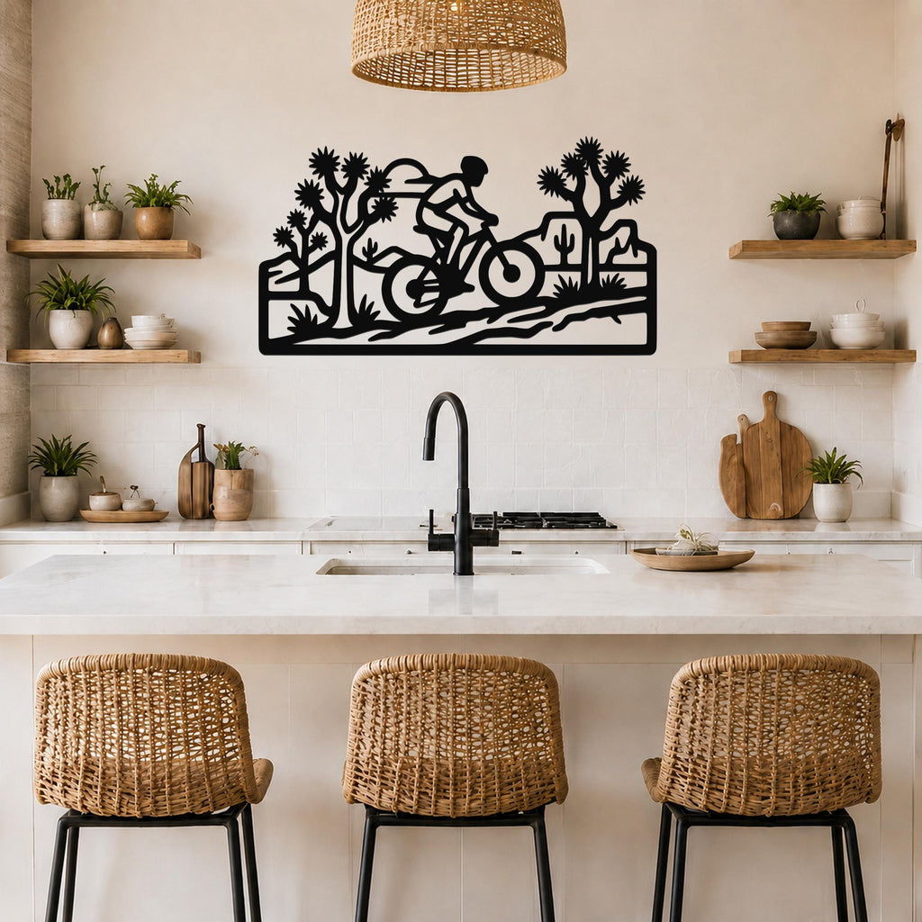 Black metal wall art cutout of a cyclist riding through a desert landscape with Joshua trees and cacti, mounted above a kitchen counter.