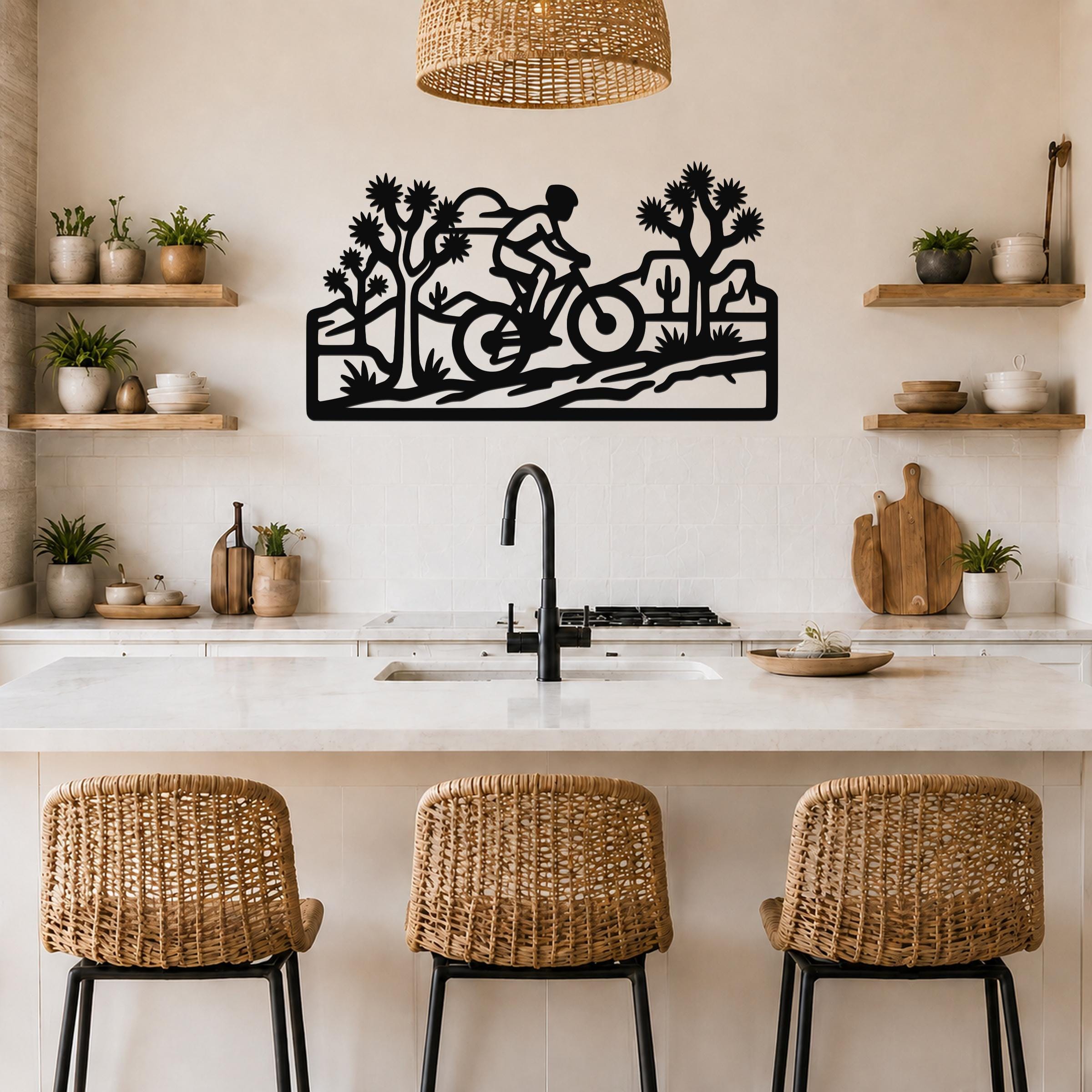 Black metal wall art cutout of a cyclist riding through a desert landscape with Joshua trees and cacti, mounted above a kitchen counter.
