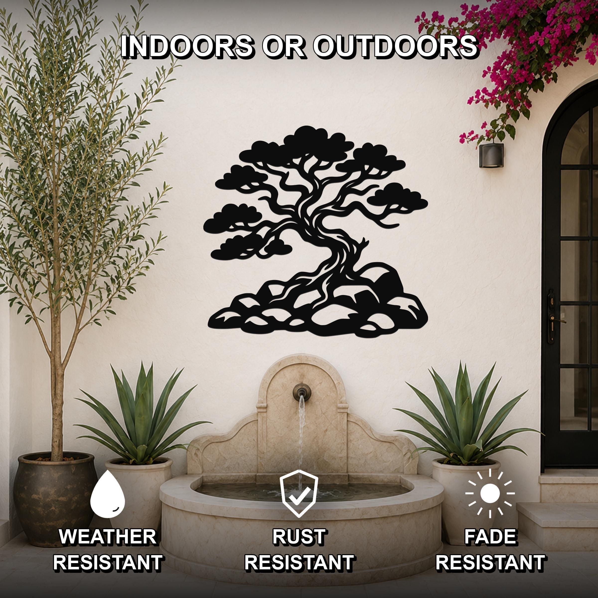 Black metal juniper tree wall art with intricate branch cutouts, mounted on an outdoor wall above a stone fountain in a patio setting.