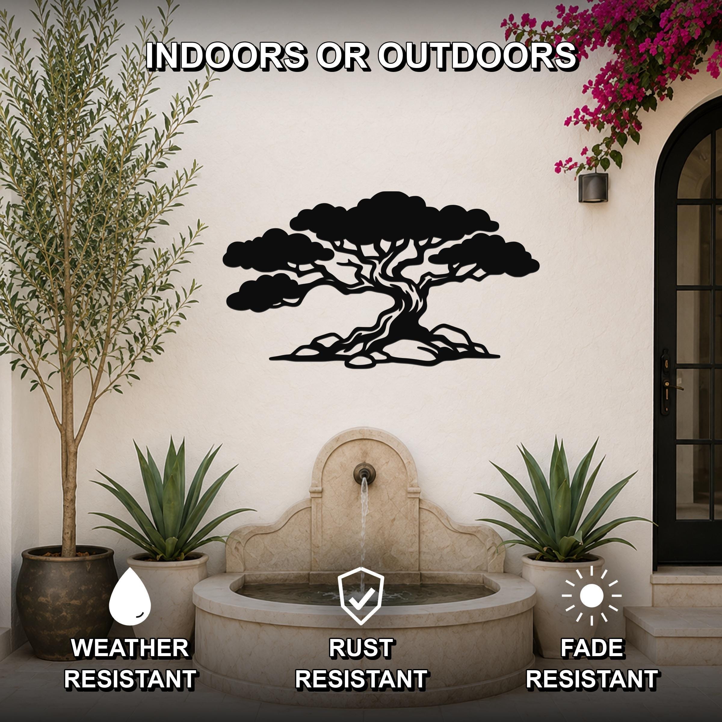Black metal juniper tree wall art with wind-sculpted silhouette, mounted on an outdoor wall above a stone fountain in a patio setting.