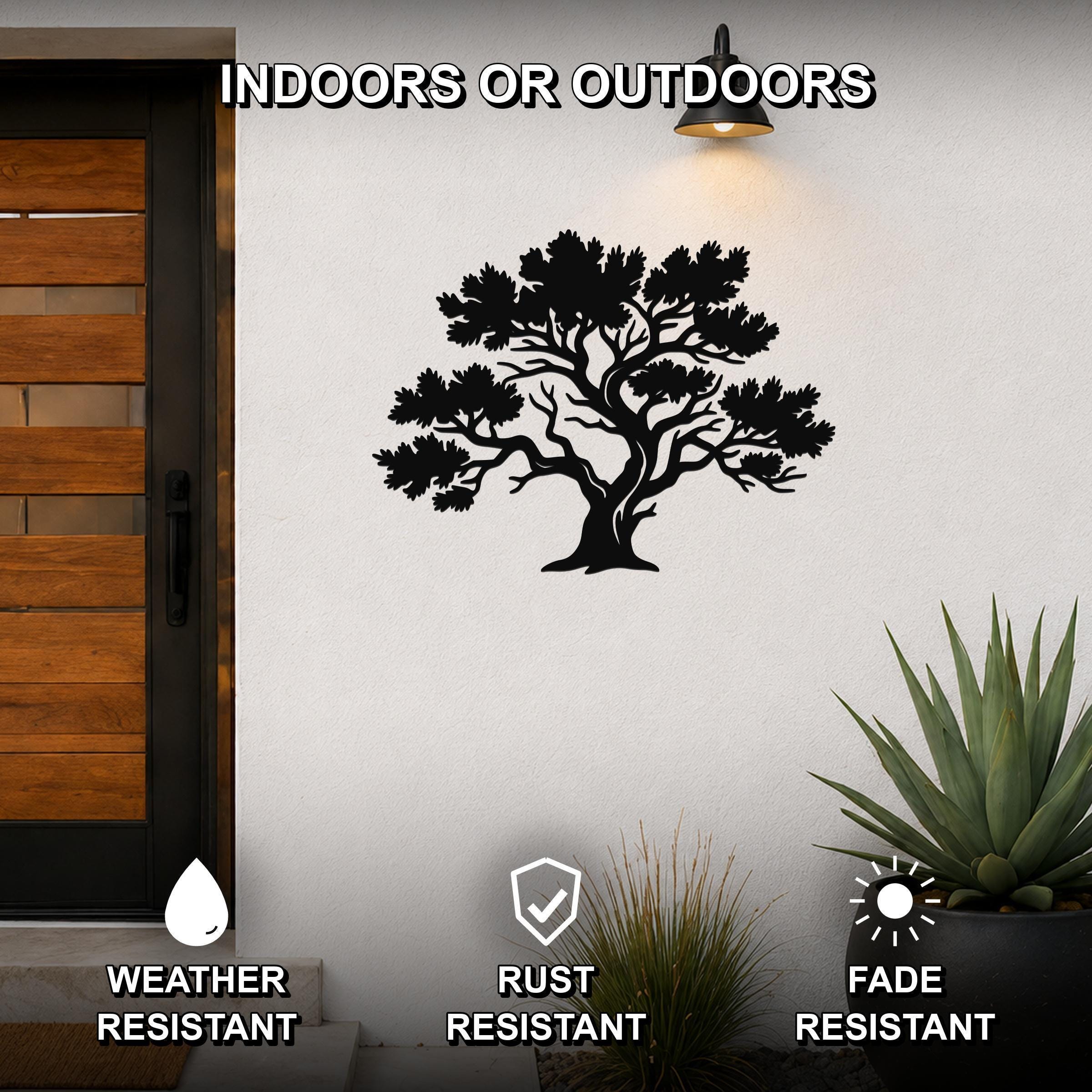 Black metal juniper tree wall art with detailed branch cutouts, mounted on an outdoor wall beside a wooden door and potted plants.