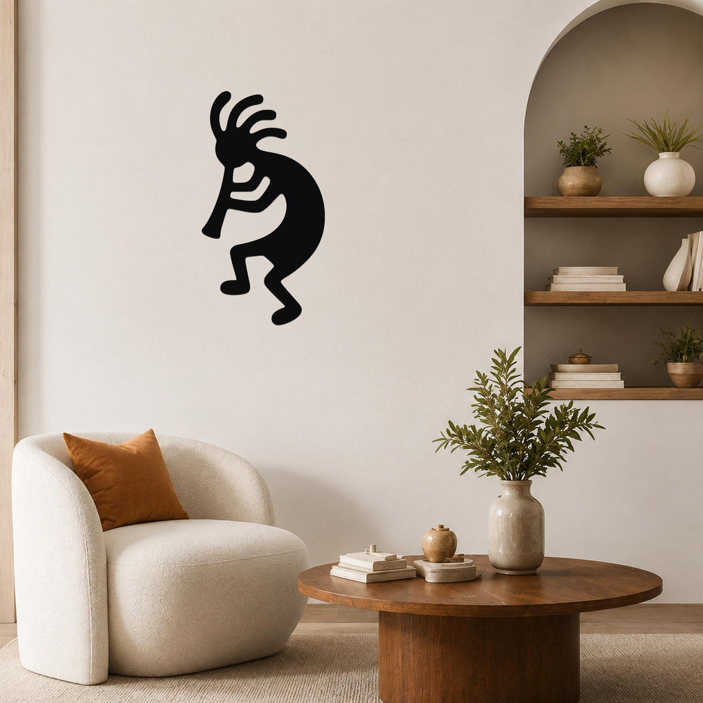 Black metal Kokopelli wall art silhouette with flute player design, mounted on a living room wall above a white armchair.