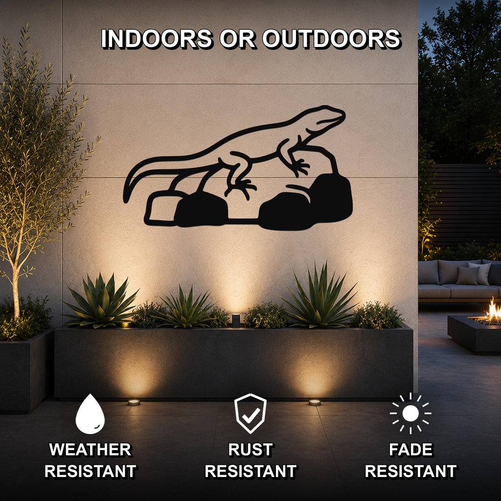Black metal lizard wall art silhouette perched on rocks, mounted on an outdoor wall above a planter in a modern patio setting.