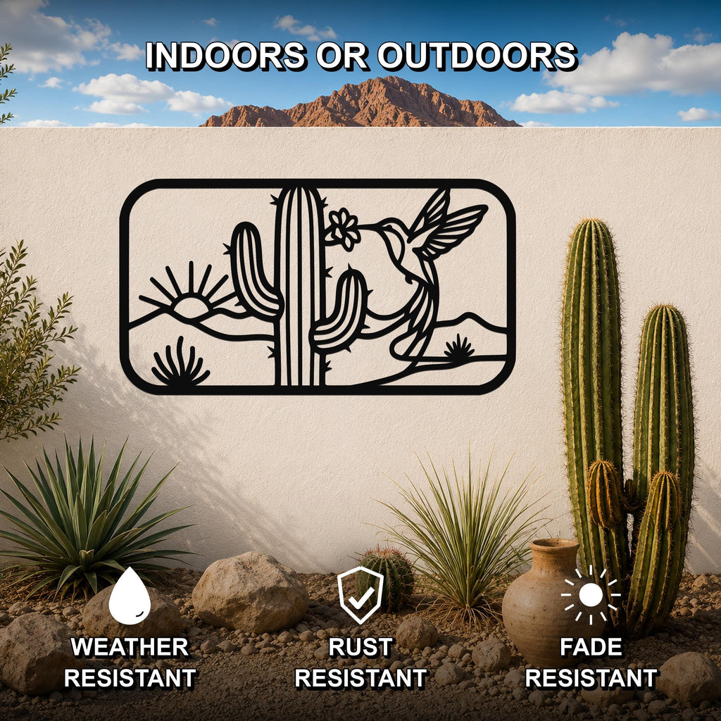 Black metal wall art with a desert scene silhouette featuring a saguaro cactus, hummingbird, and sun, mounted on an outdoor wall above a rock and cactus garden.