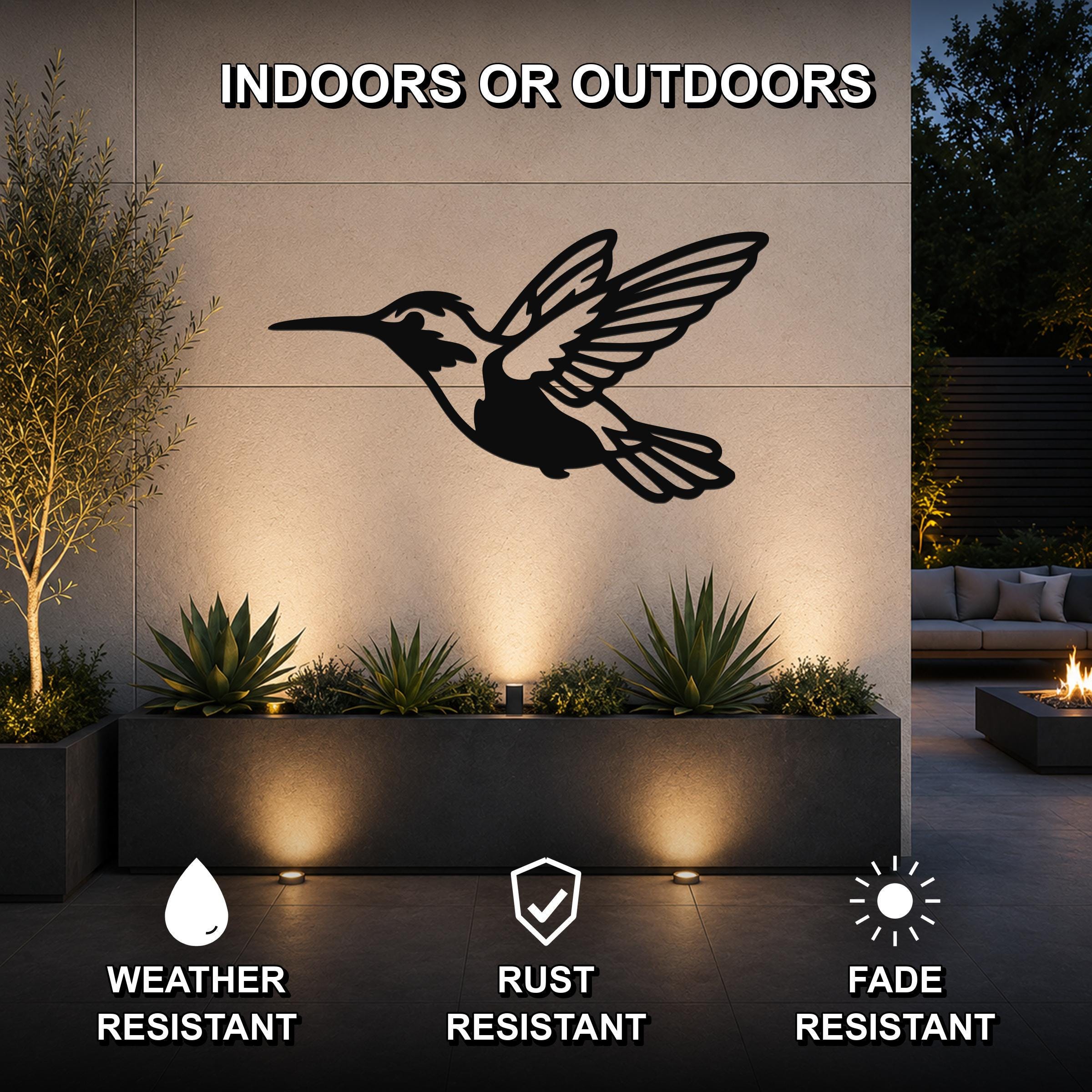 Black metal hummingbird wall art with wing and tail cutouts, mounted on an outdoor wall above a planter in a patio setting.