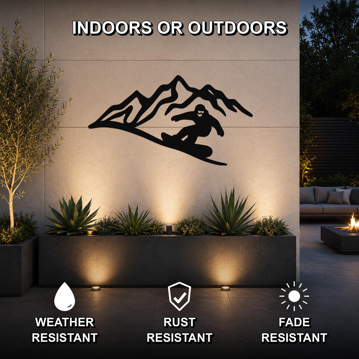 Black metal wall art featuring a snowboarder silhouette in front of mountain peaks, mounted on an outdoor wall above a planter with uplighting.