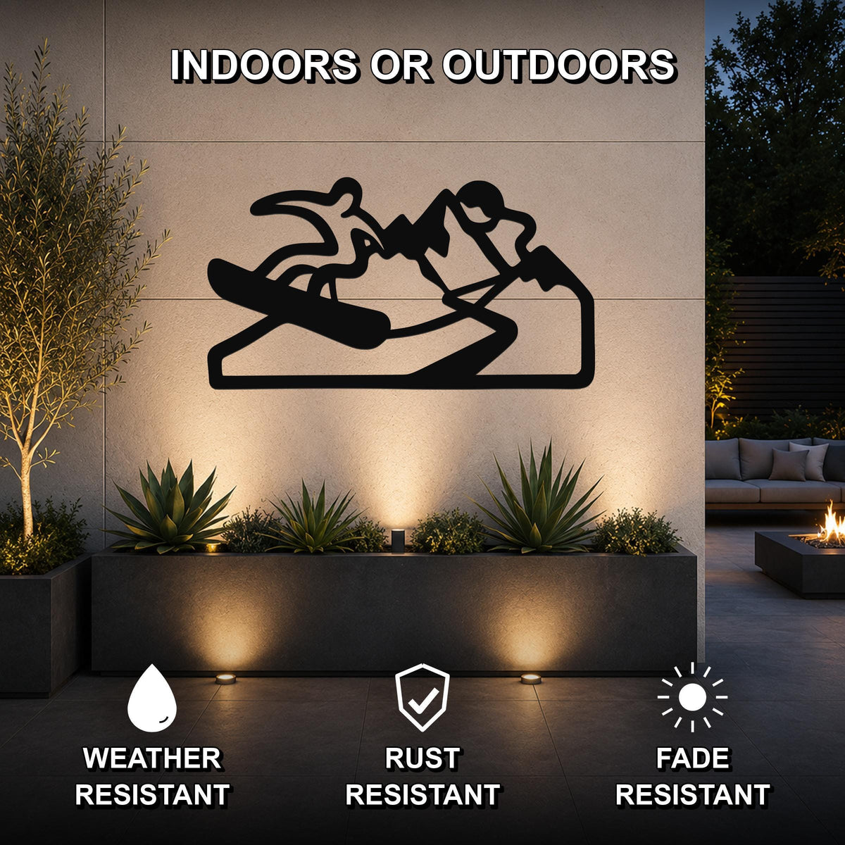 Black metal wall art silhouette of a snowboarder on a mountain, mounted on an outdoor wall above a planter in a patio setting.