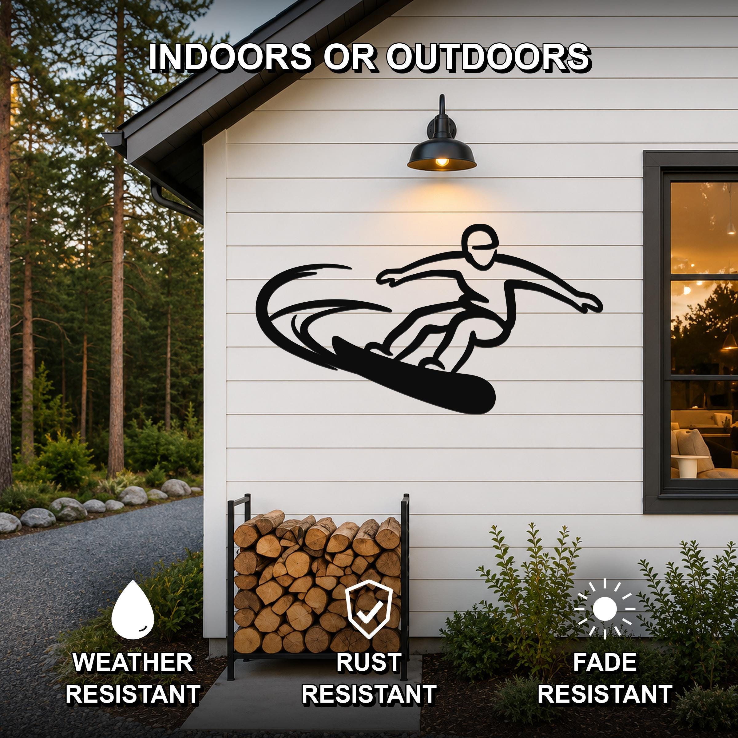 Black metal wall art featuring a snowboarding silhouette with motion lines, mounted on a white exterior wall above a firewood rack.