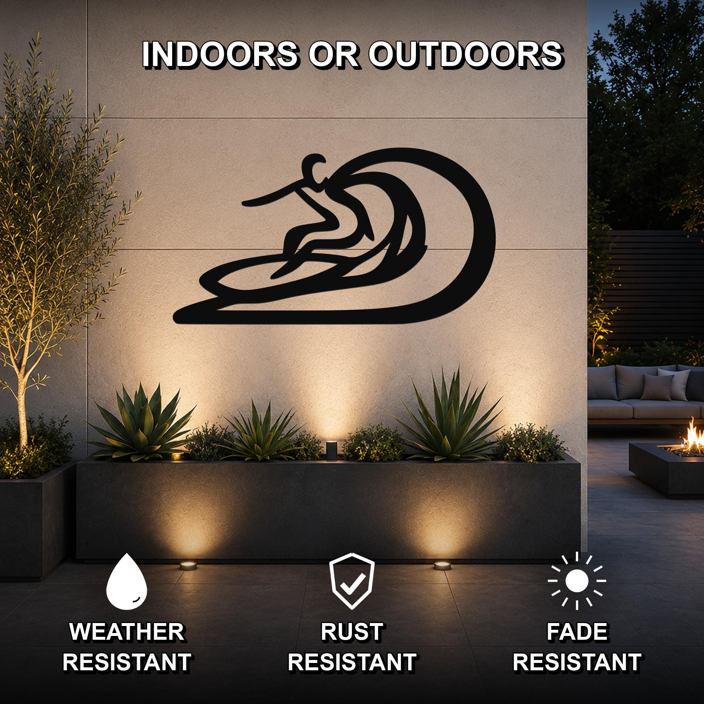 Black metal surfer wall sculpture with wave cutout, mounted on an outdoor wall above a planter in a patio setting.