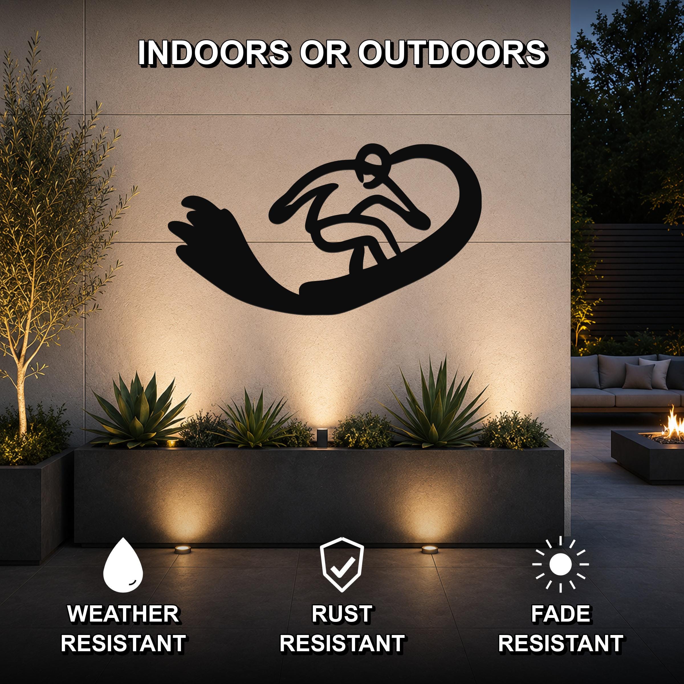 Black metal wall art of a snowboarder silhouette with motion lines, mounted on an outdoor wall above a planter in a modern patio setting.