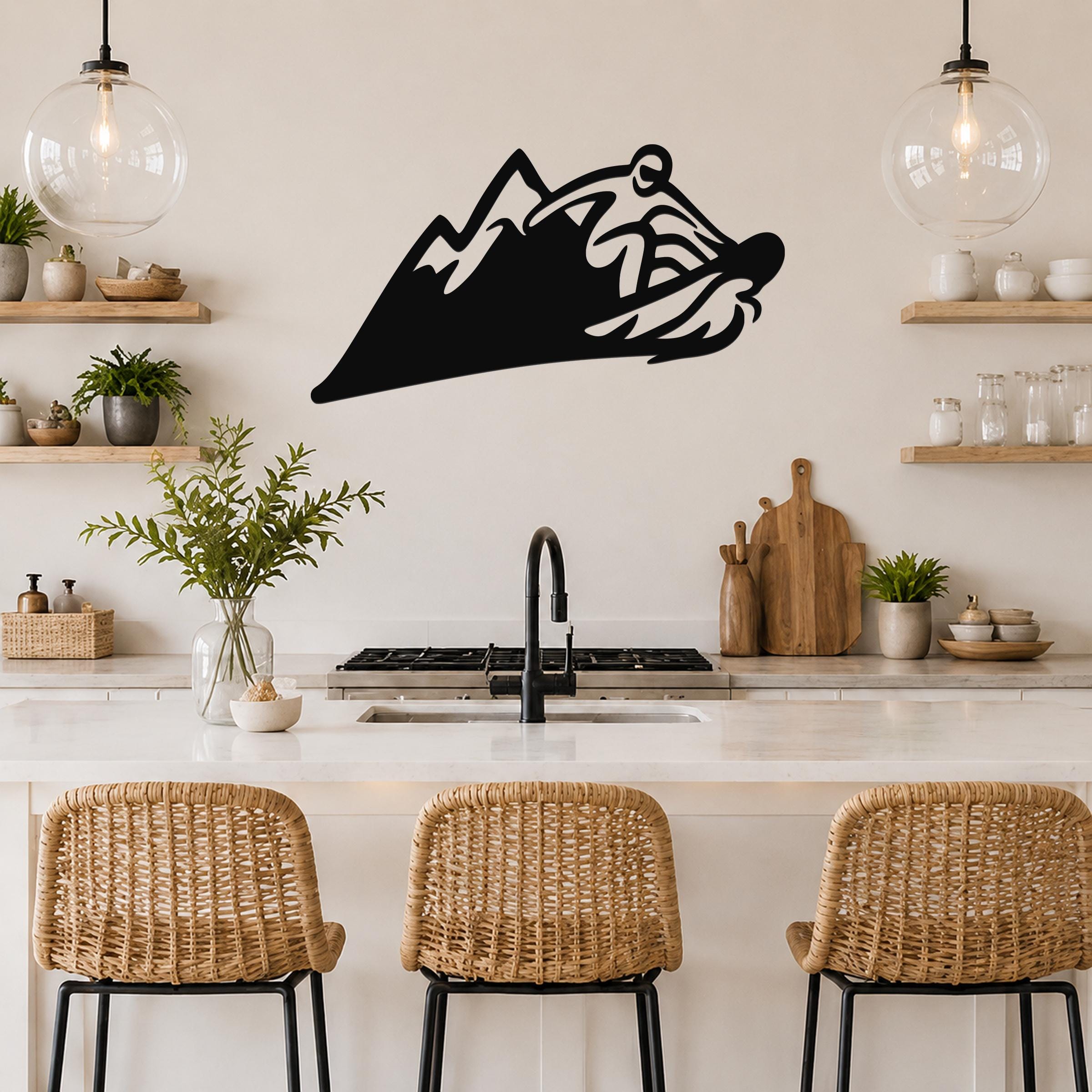 Black metal wall art featuring a snowboarder silhouette in motion, mounted above a kitchen counter with wicker bar stools and open shelving.