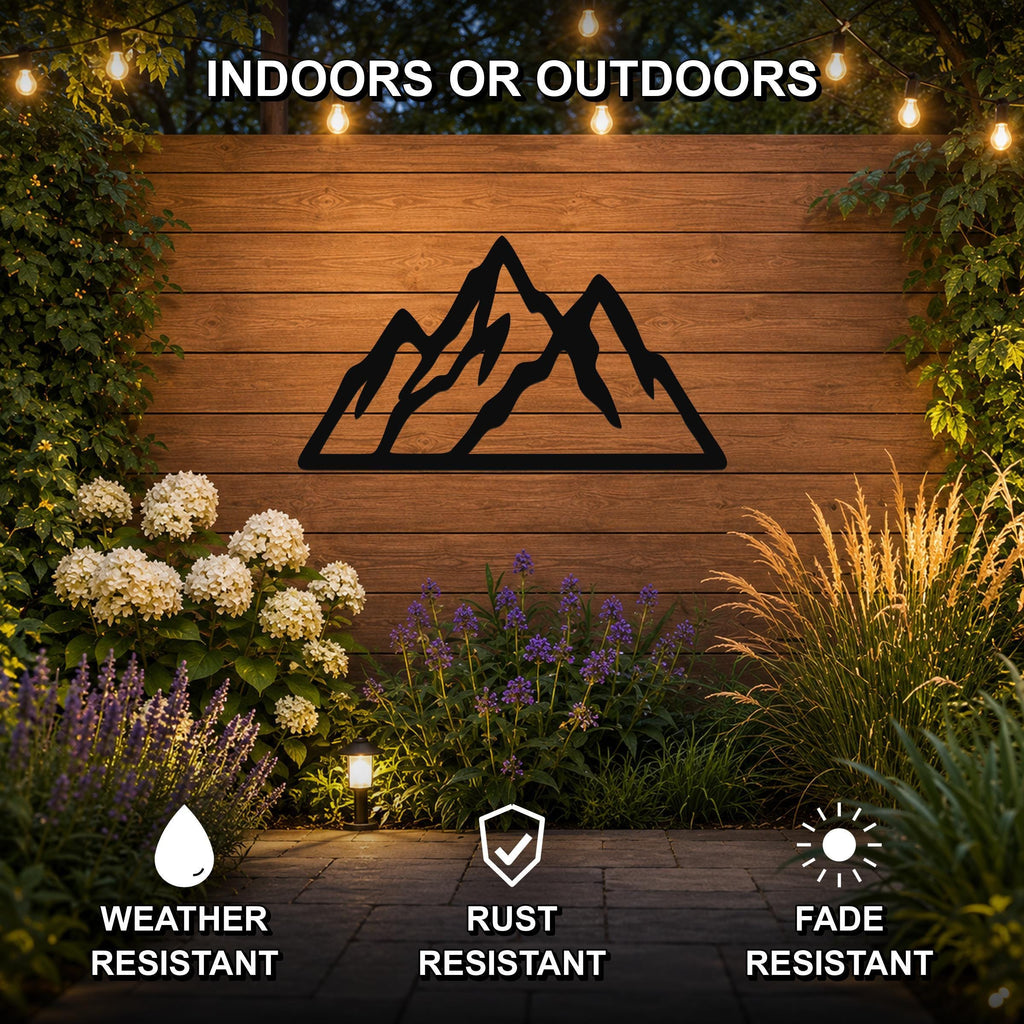 Black metal mountain silhouette wall art mounted on a wooden outdoor wall, surrounded by plants and string lights, with icons indicating weather, rust, and fade resistance.