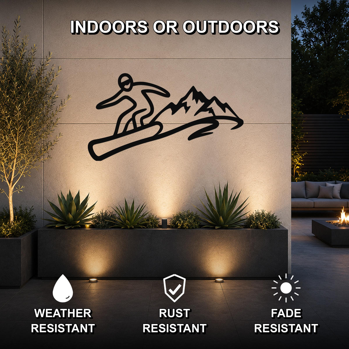 Black metal wall art featuring a snowboarder silhouette in motion above mountains, mounted on an outdoor wall above a planter in a patio setting.