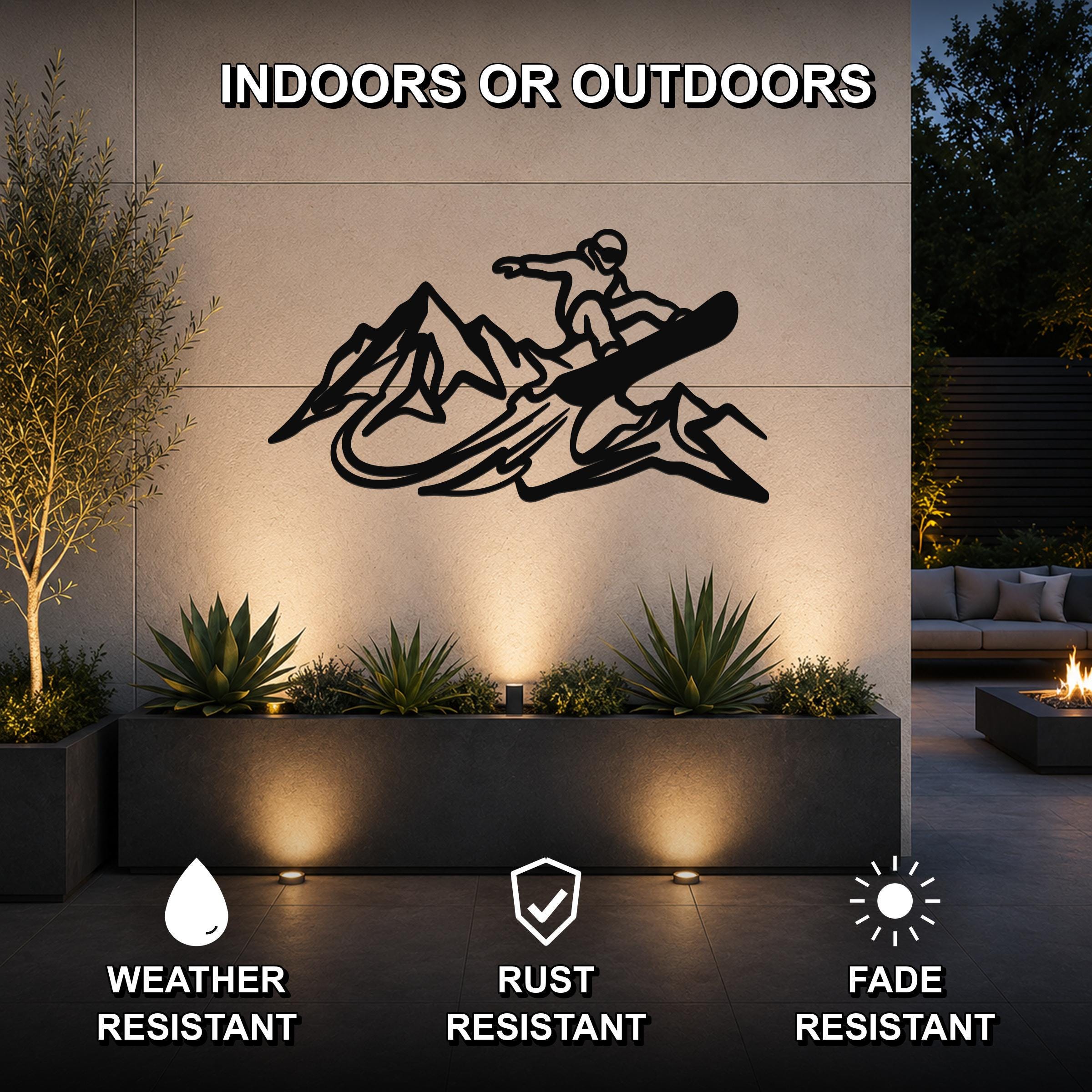 Black metal wall art featuring a snowboarder silhouette over mountain peaks, mounted on an outdoor wall above a planter in a modern patio setting.