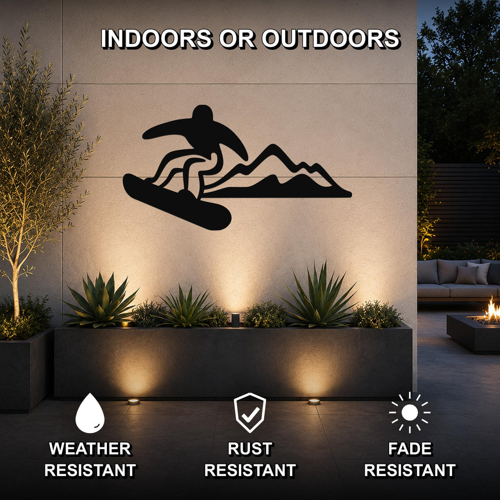 Black metal wall art featuring a snowboarder silhouette in motion above mountain peaks, mounted on an outdoor wall above a planter in a modern patio setting.