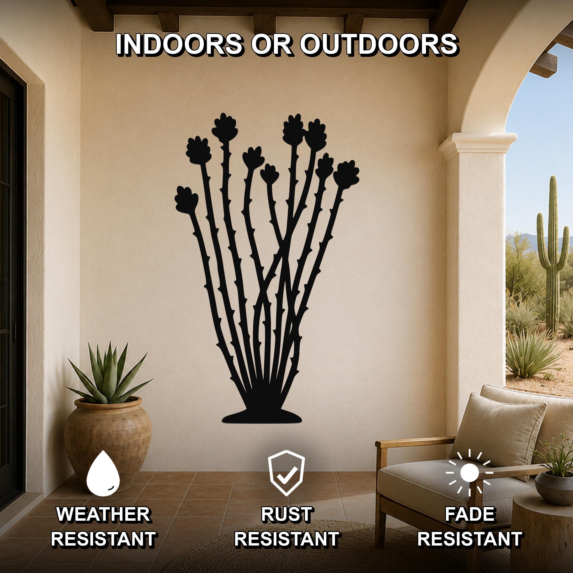 Black metal ocotillo wall art with spiny stems and flower cutouts, mounted on a beige patio wall above a chair, shown in an indoor-outdoor setting.