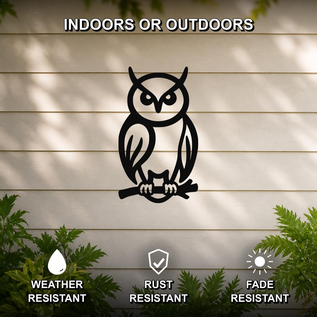 Black metal owl wall art in a silhouette style, perched on a branch, mounted on a light-colored outdoor wall with greenery below.