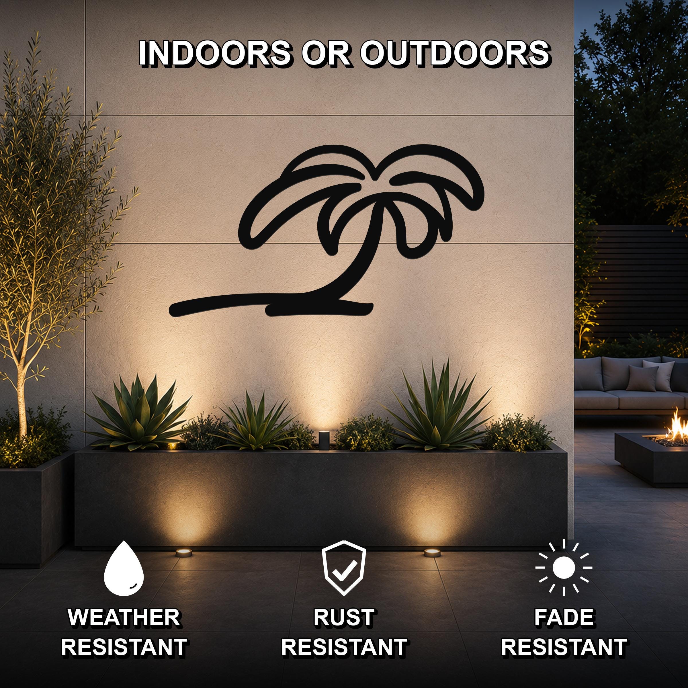 Black metal palm tree wall art with a silhouette design, mounted on an outdoor wall above a planter in a patio setting.
