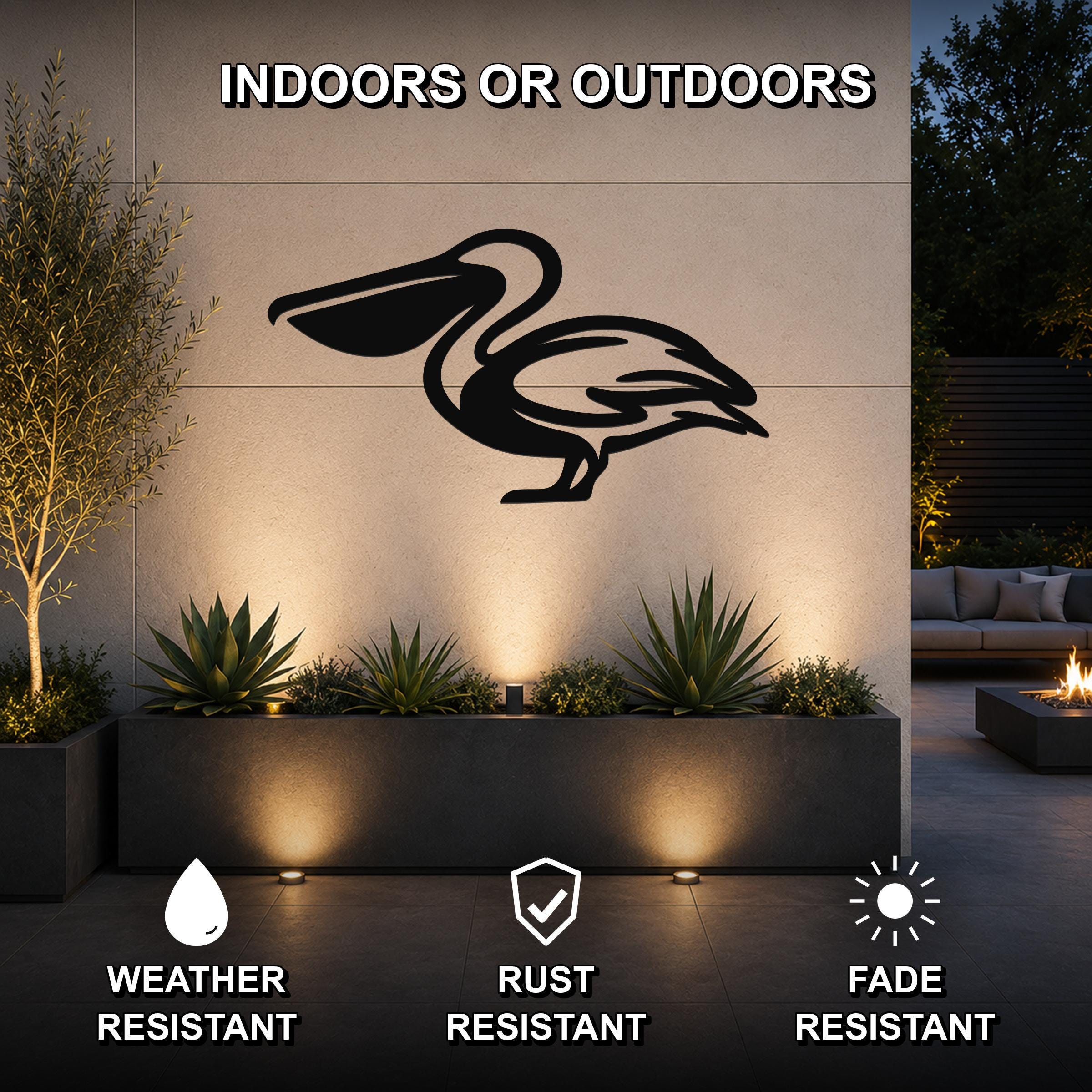 Black metal pelican wall art silhouette mounted on an outdoor wall above a planter, illuminated by uplights in a modern patio setting.