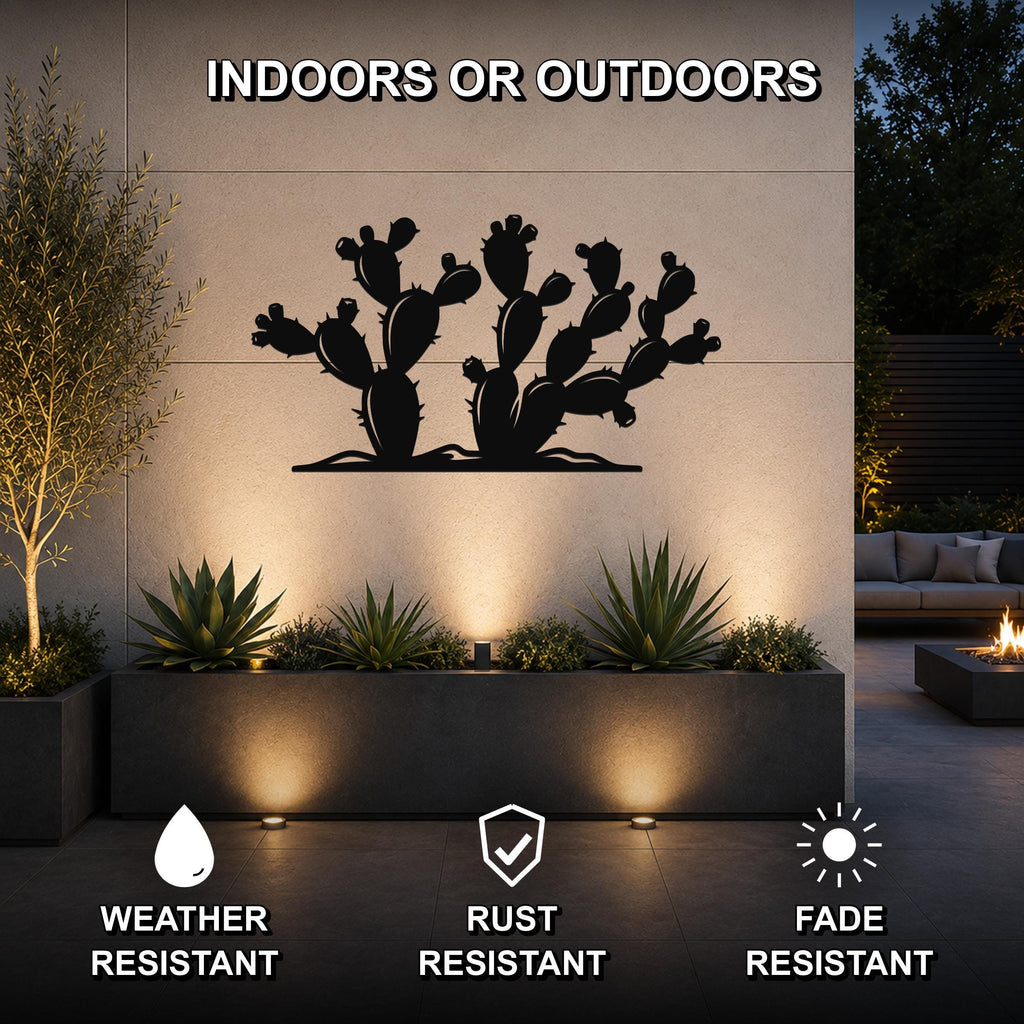 Black metal cactus wall art with multiple paddle-shaped segments and spines, mounted on a beige outdoor wall above a planter with succulents, illuminated by uplighting.